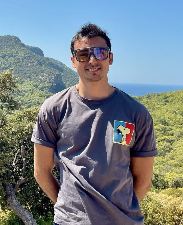 Parsa Payandeh outdoors, smiling, with forested hills and the sea behind him